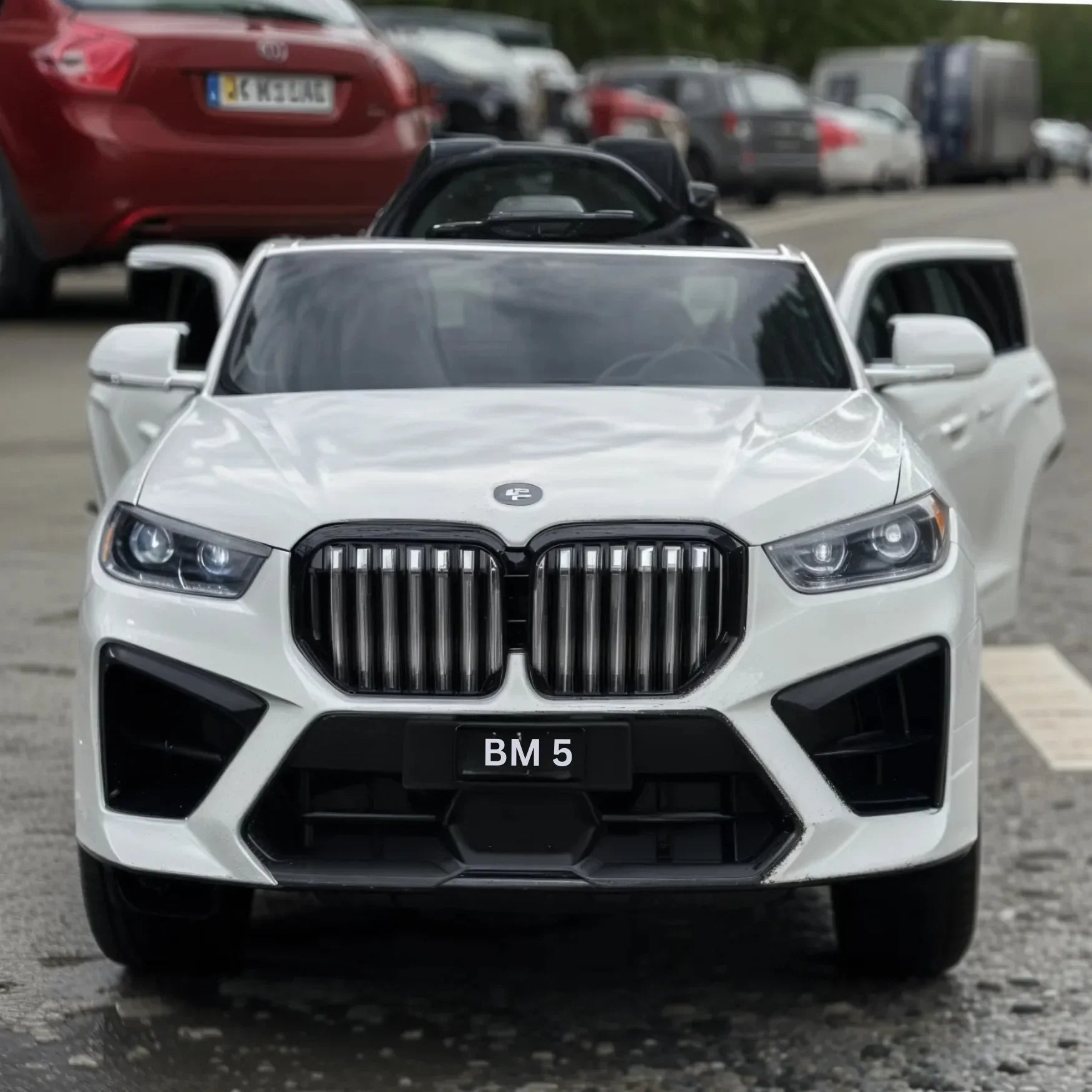 White toy car resembling a BMW X5 in a parking lot with other cars.